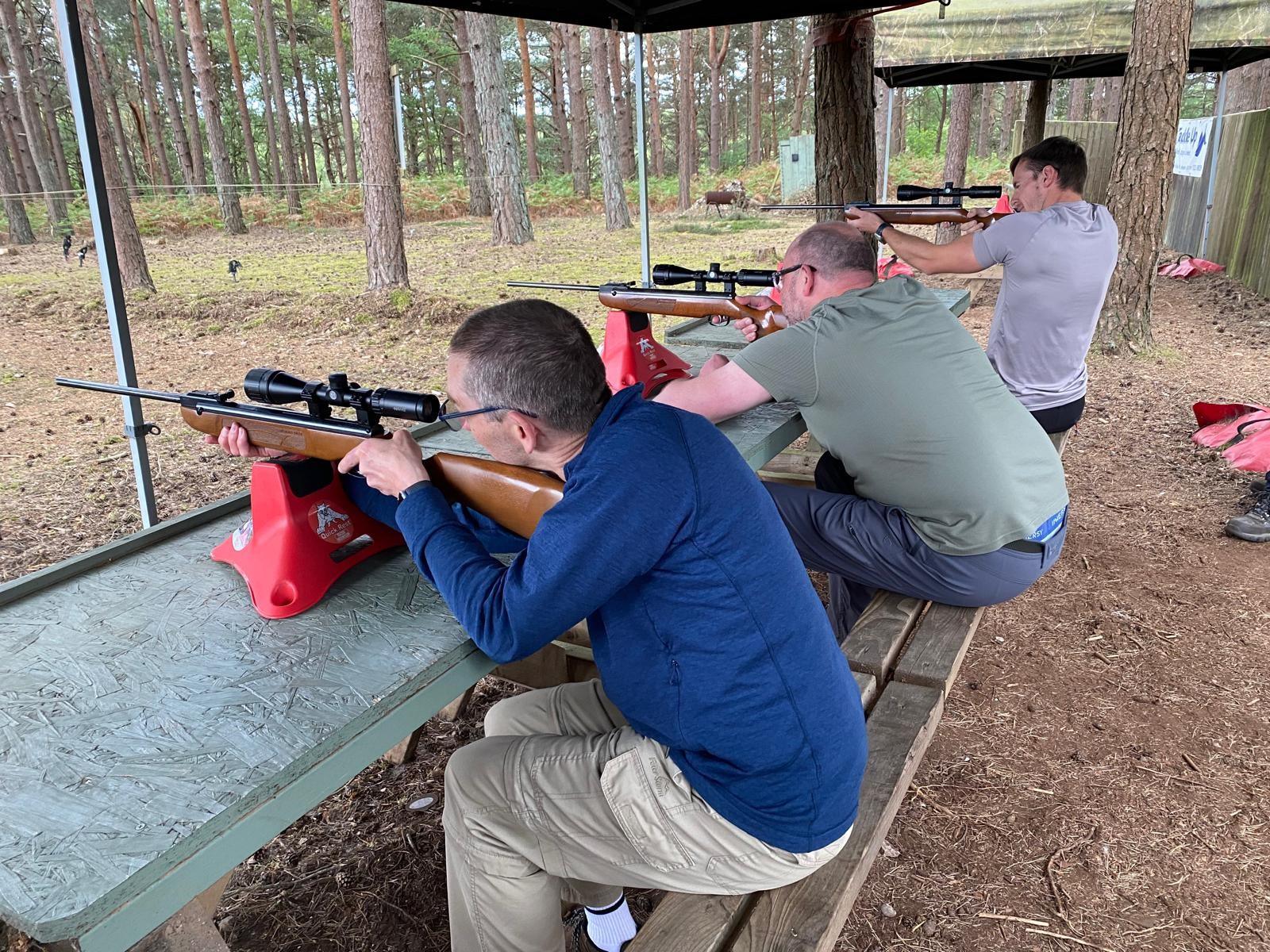 Three shooters lined up at the covered .22 rifle range with scoped rifles on rests