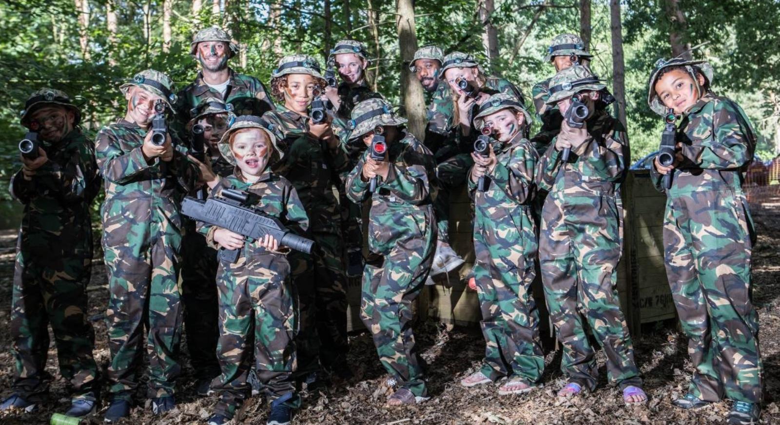 Children and an adult in camouflage kit posing with laser rifles before a game