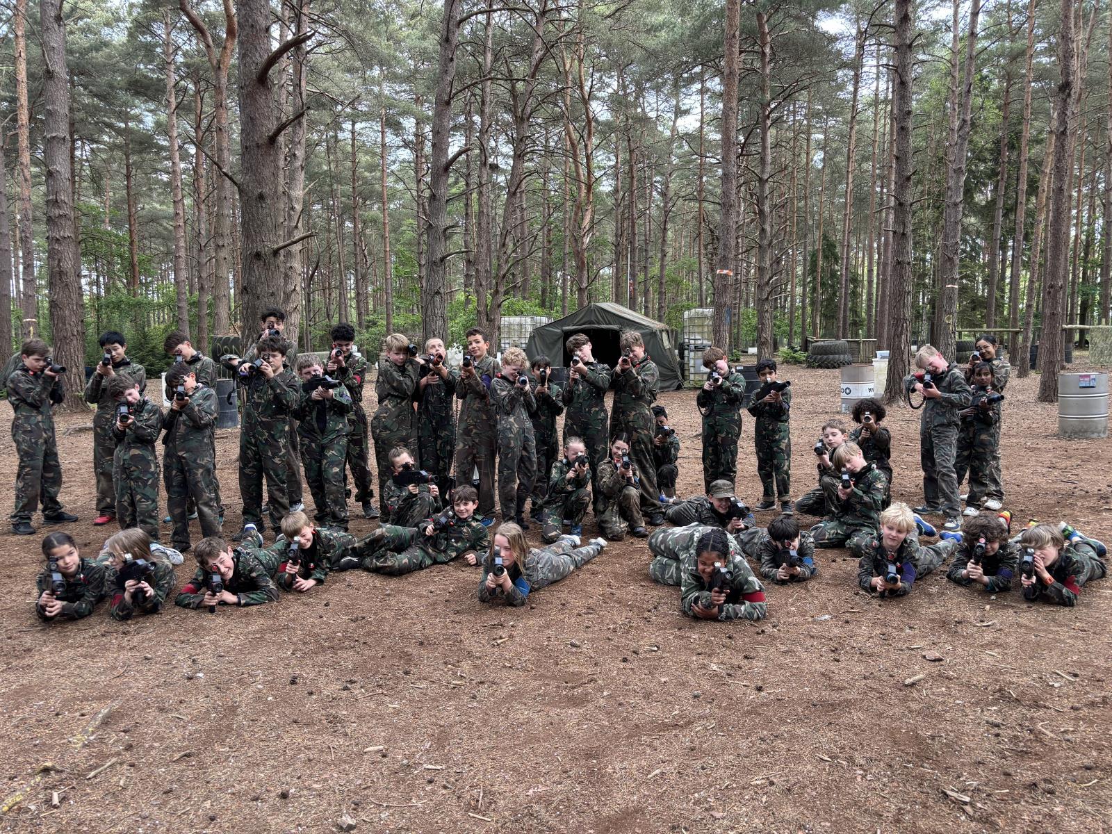 A large group of children in camouflage taking aim with laser rifles in woodland
