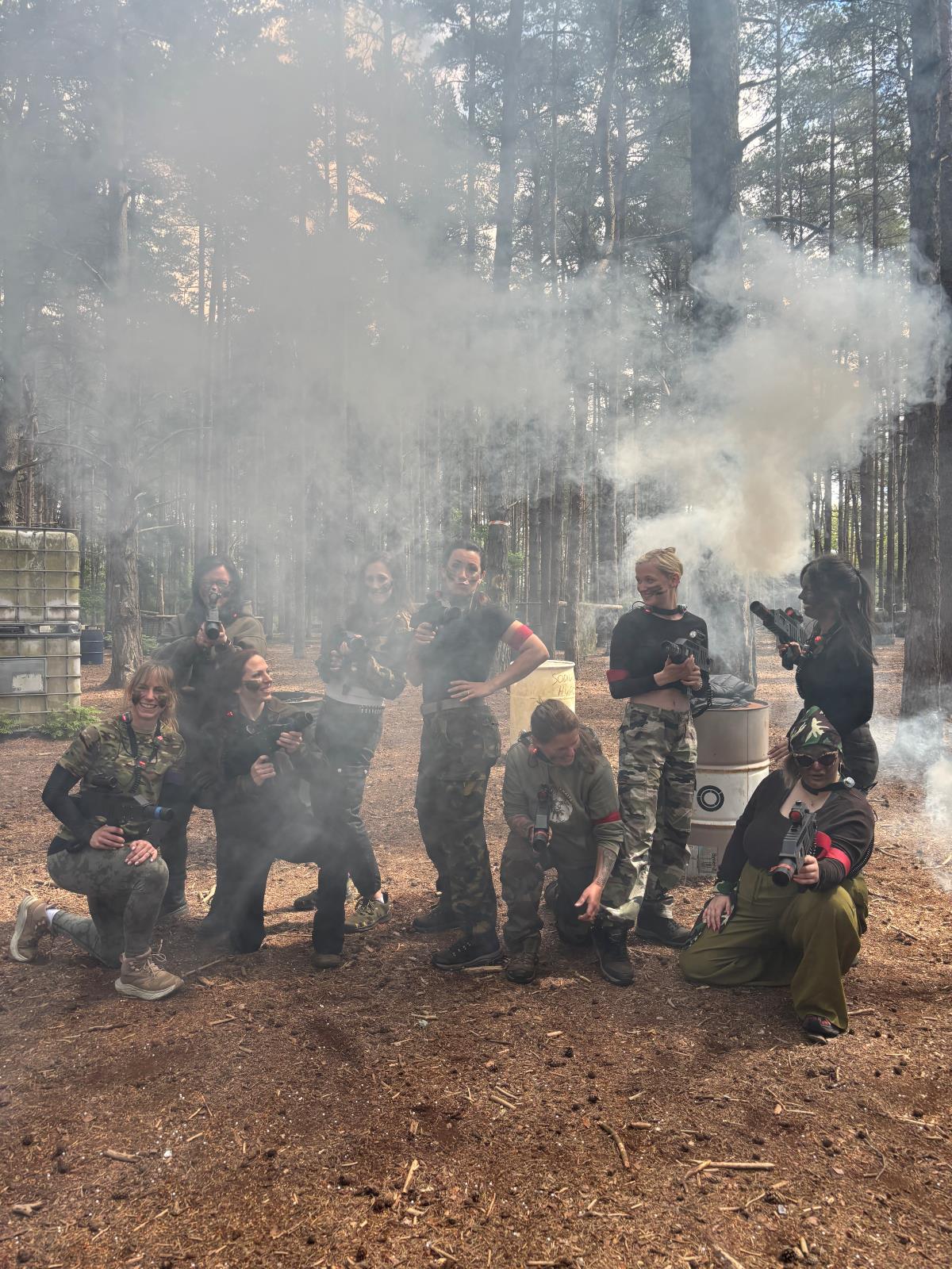 Adult hen party group in camouflage kit surrounded by smoke during a laser tag game