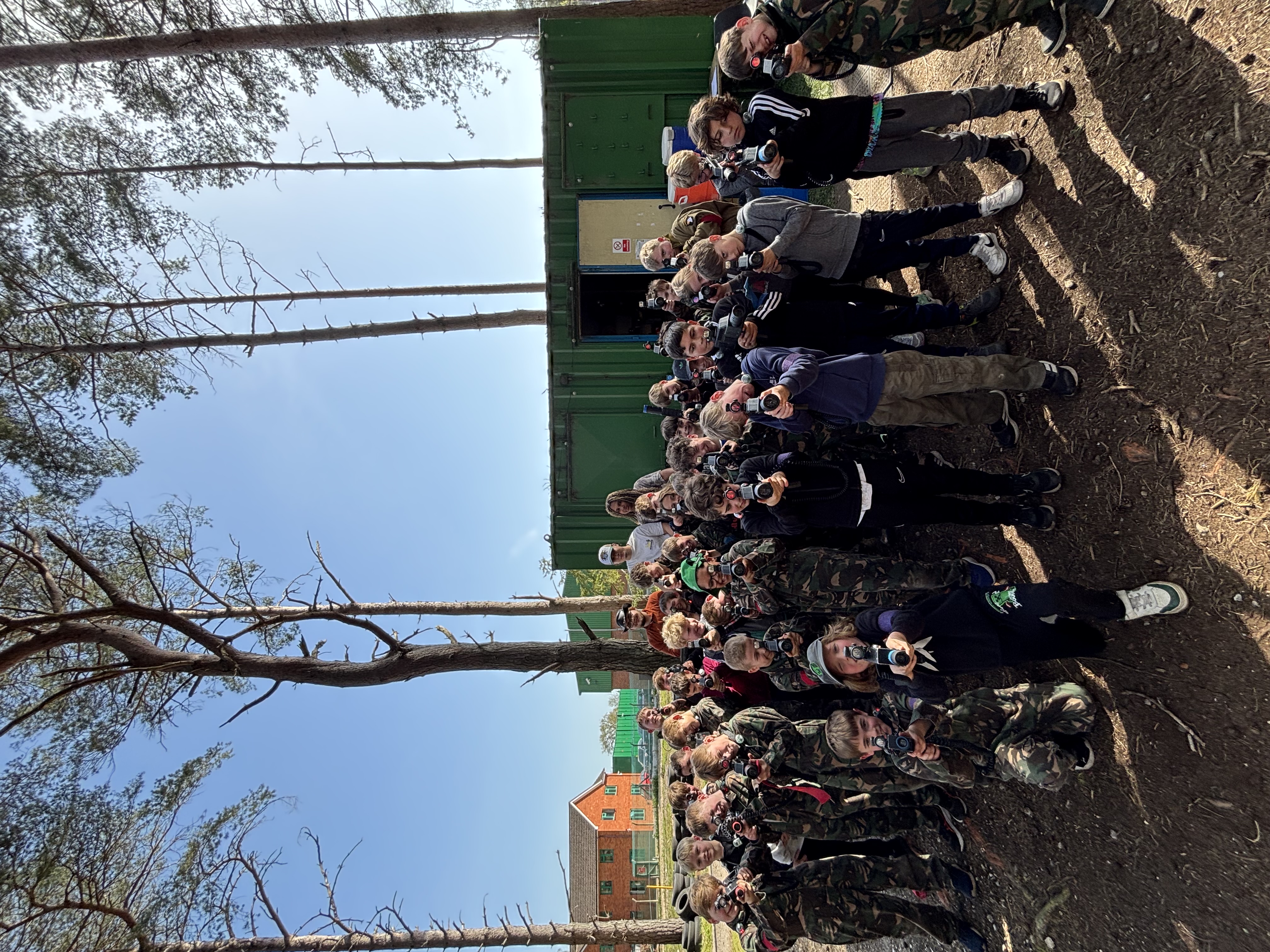 A large school group in camouflage overalls with laser rifles before a session