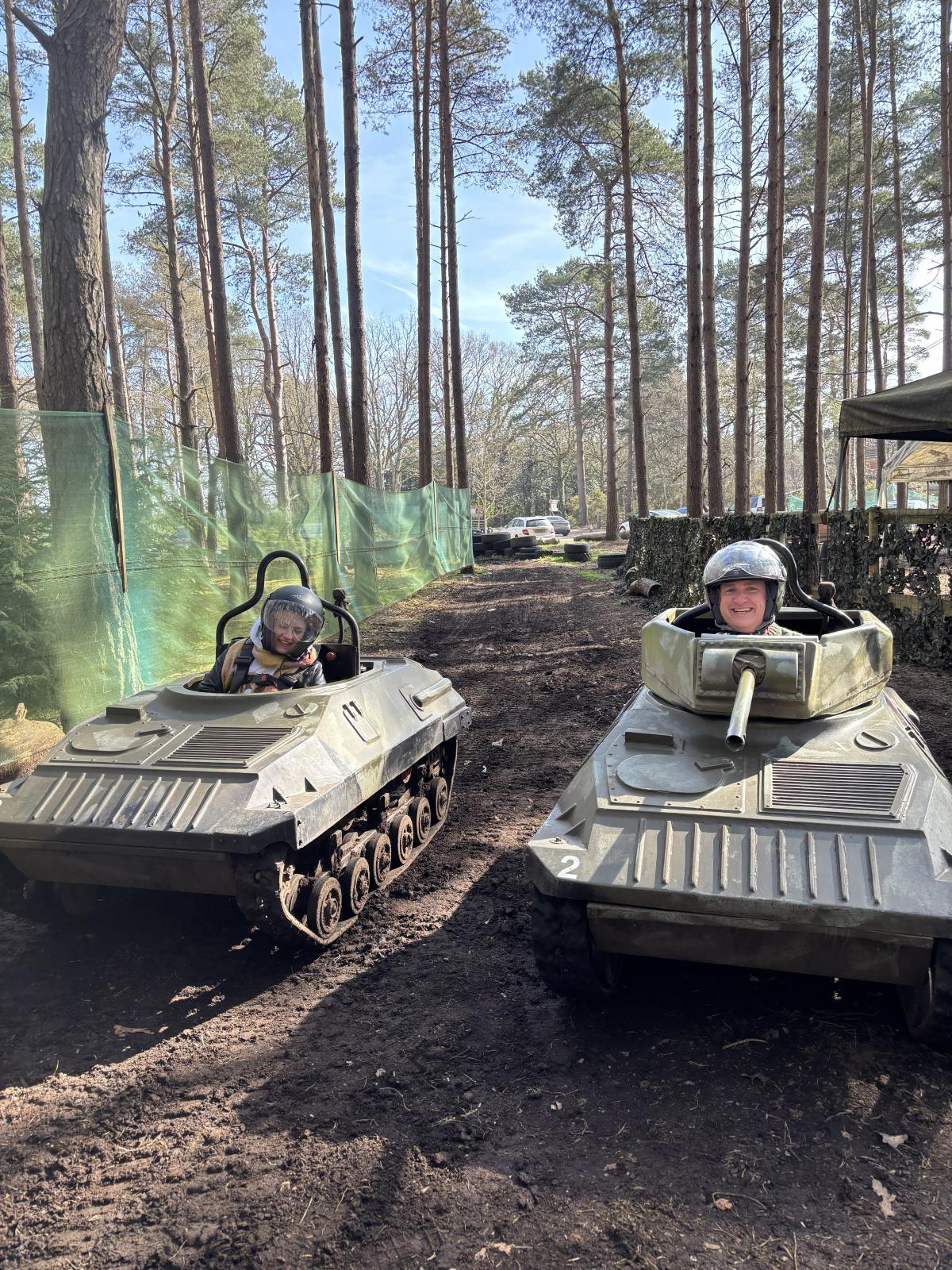 Two drivers grinning from the cockpits of one-person mini tanks on a woodland track